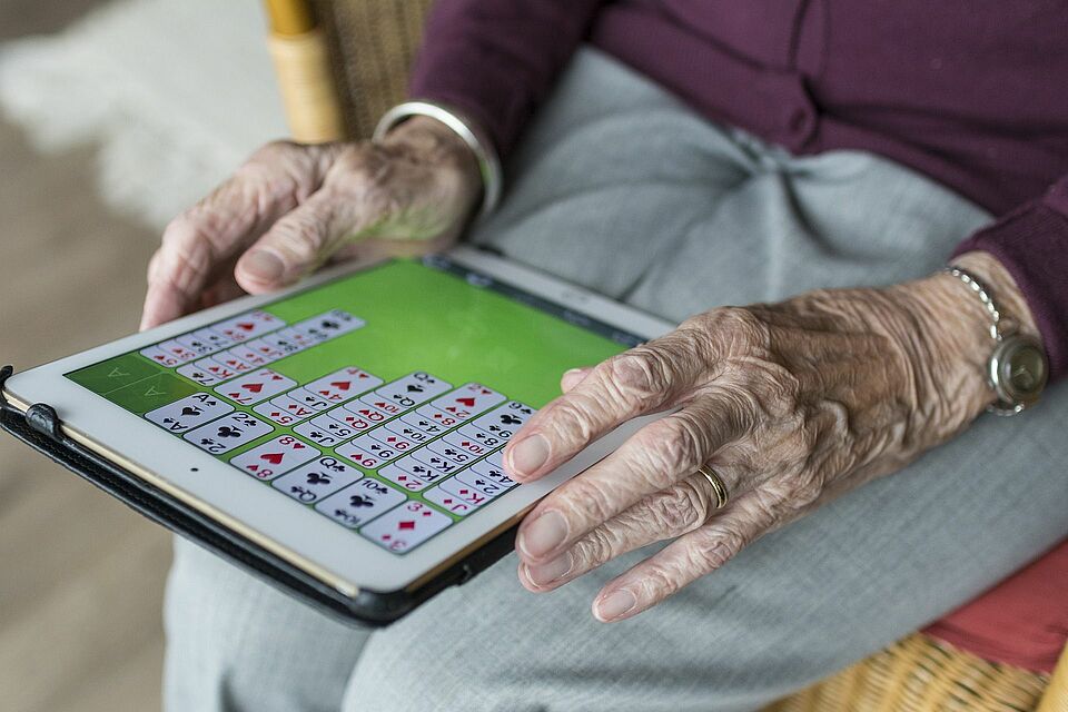 Seniorin mit Tablet spielt ein digitales Kartenspiel 